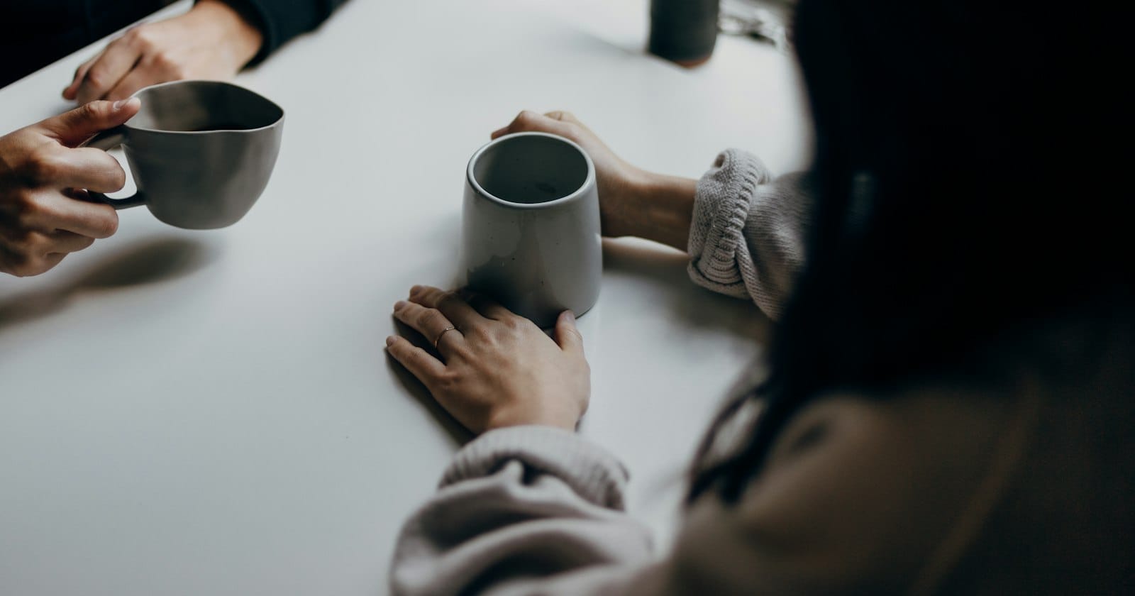 Two people in conversation across a table with coffee cups, suggesting a one-on-one advisory meeting